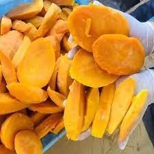 A gloved hand holding slices of vibrant frozen mango.